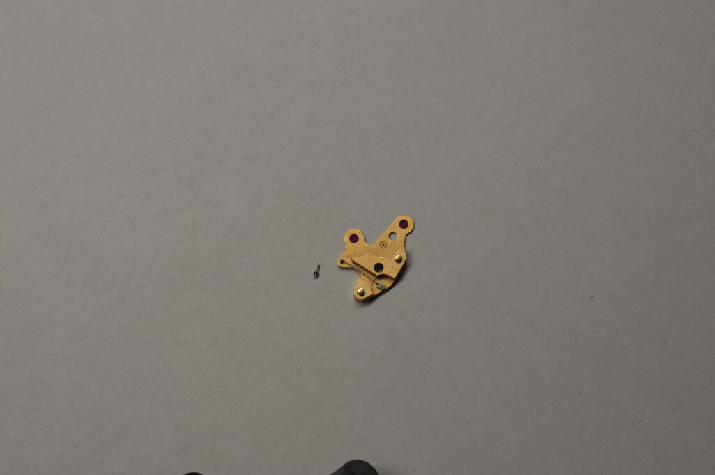 Engraved cock from calibre 861 beside a small pivot pin